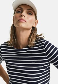 Marineblå og hvid stribet t-shirt med rund hals, der har "GANT" logoet i hvidt på brystet og korte ærmer.