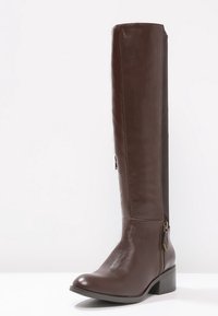 Bota de cuero marrón hasta la rodilla con una textura suave, cremallera lateral y un tacón bloque. Presenta un panel elástico para ajustar el ajuste.