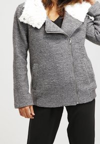 Grå zip-up jacka med en texturerad ullkropp, vit fleecekrage, sidofickor och ribbade manschetter, som erbjuder en mysig och varm design.