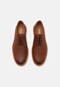 Chaussures en cuir marron à lacets avec des bouts arrondis, des coutures contrastantes plus claires et une semelle en caoutchouc texturée. Présente une finition lisse.