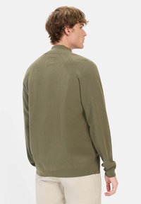 Olivenfarvet strikket sweater med høj krave, ribbet struktur og diskret detaljering på ryggen. Lange ærmer, afslappet pasform.
