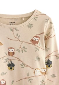 Beige Kinderhemd mit langen Ärmeln, bedruckt mit braunen und weißen Eulen, Baumzweigen, grünen Blättern und hängenden Vogelhäuschen. Größenetikett innen am Kragen.