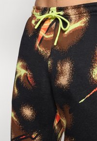 Drawstring sweatpants in a multicolored print featuring brown, black, and neon accents. Soft fabric with a textured, graphic design.
