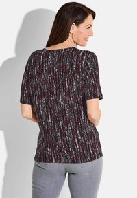 Kurzarmoberteil aus strukturiertem Stoff mit einem schwarzen, roten und grauen Muster. Verfügt über einen runden Ausschnitt und einen abgerundeten Saum hinten.