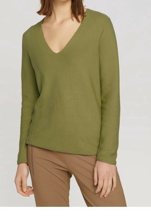 Olivgrüner V-Ausschnitt-Pullover mit langen Ärmeln, strukturiertem Strickgewebe und lockerer Passform. Kombiniert mit hellbraunen, strukturierten Hosen.