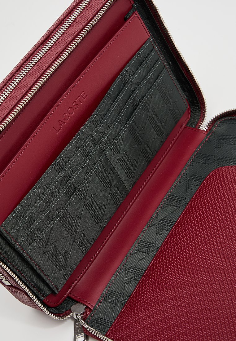 Portefeuille en cuir rouge avec fermeture zippée, compartiments pour cartes intérieurs en tissu noir avec un motif texturé et une marque en relief.