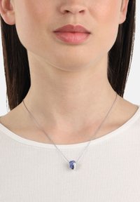 Silver necklace with blue and white stones in a twisted knot design, resting on a white, ribbed shirt.