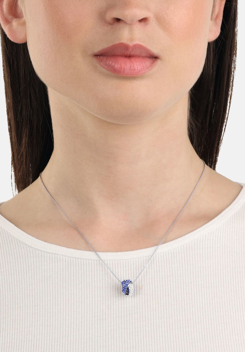 Silver necklace with blue and white stones in a twisted knot design, resting on a white, ribbed shirt.