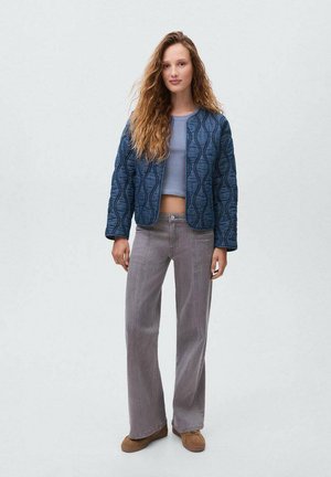 Giacca blu trapuntata con un motivo a onda, abbinata a un top azzurro chiaro e jeans grigi a gamba larga. Footwear marroni completano l'outfit.