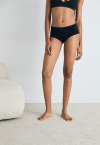 Black seamless bra and matching high-waisted briefs displayed on a model. The fabric appears soft with a smooth texture.