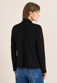 Schwarze Blazer mit langen Ärmeln und Kragen, glatte Textur und maßgeschneiderte Passform, kombiniert mit blauen Jeans.