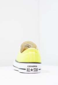 Żółte płócienne trampki z białymi szwami, czarną gumową podeszwą i logo "Converse All Star" na pięcie. Okrągły nosek, niski krój.