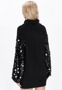 Rochie tricotată neagră cu o textură pufoasă, guler înalt și mâneci voluminoase decorate cu paiete negre strălucitoare.