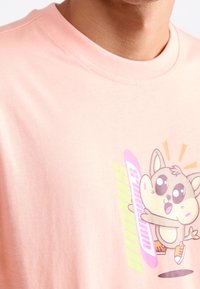 Rosa bomullströja med en tecknad karaktärsgrafik med stora ögon och lekfull pose. Korta ärmar, rund halsringning, mjuk textur.