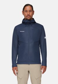 Tamsiai mėlynas softshell švarkas su užtrauktuku, reguliuojama kapišonu ir dviem šoninėmis kišenėmis. Yra logotipas ant krūtinės ir rankovės, maloni tekstūra.