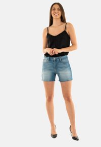 Camisón de satén negro con tirantes de cuentas, combinado con pantalones cortos de denim azul claro y tacones altos negros. Ajuste slim y estilo casual.