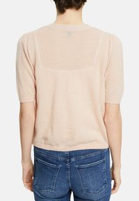 Hellrosa gestrickter Pullover mit kurzen Puffärmeln, geripptem Saum und einem durchsichtigen Rückenteil. Kombiniert mit blauen Jeans.