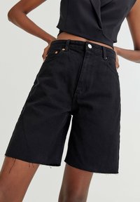 Shorts in denim nero con vita medio-alta, caratterizzati da un taglio dritto, orlo sfrangiato e dettagli in metallo a contrasto davanti.
