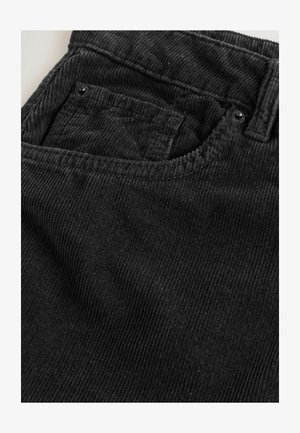 Tissu en velours côtelé noir avec une texture à nervures verticales, présentant une petite poche avec un bouton en métal noir et une taille visible.