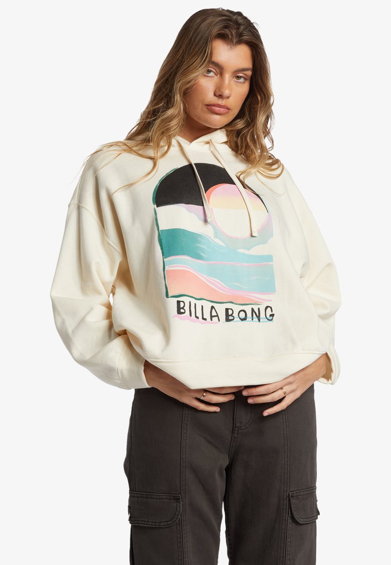 Hoodie color crema con una grafica frontale che presenta onde astratte e un sole. Caratterizzato da una vestibilità ampia, cappuccio con cordoncino e texture morbida.
