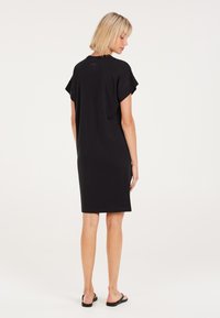 Schwarzes Baumwollkleid mit kurzen Ärmeln, Rundhalsausschnitt und knielangem Design. Glatte Textur, minimalistischer Stil ohne sichtbare Muster oder Metallteile.