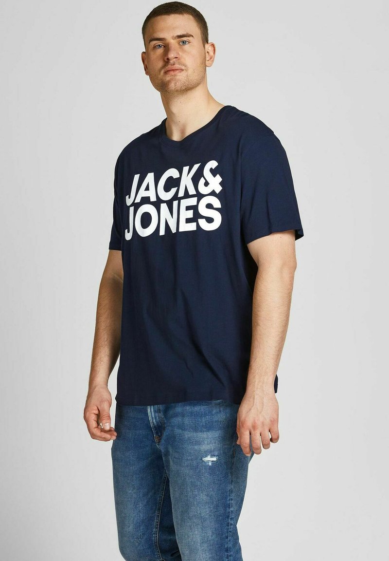 Navy blue cotton t-shirt with a crew neck and short sleeves. Features large white text "JACK&JONES" on the front. Worn with blue distressed jeans.