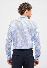 Lichtblauw overhemd met lange mouwen met een geometrisch patroon, met knoopmanchetten, kraag en een rechte zoom. Draagt bij donkere broeken.