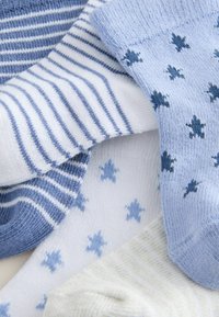 Patru perechi de șosete în nuanțe variate de albastru, alb și crem. Caracteristicile includ dungi, modele cu stele și diferite texturi.