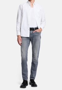 Camisa blanca de botones, vaqueros de mezclilla gris, cinturón negro y zapatos negros. Corte ajustado con textura suave y diseño clásico de cuello.