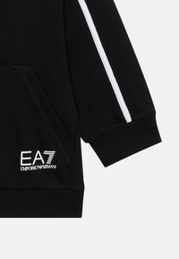 Svart hettegenser med en myk tekstur, med en hvit stripe langs ermet og et brodert logo på fronten.