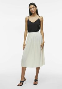 Top senza maniche nero abbinato a una gonna plissettata leggera, lunga fino al ginocchio. La modella indossa sandali con tacco neri. Design semplice ed elegante.