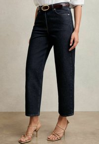 Mörkblå högmidjade jeans med rak benpassform, minimalt sömnad och framfickor. Bärs med ett brunt bälte och beige klackar med remmar.