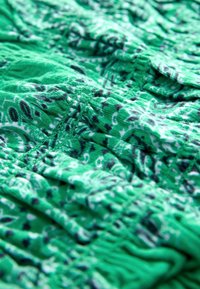 Tissu vert avec motifs paisley blancs et noirs, montrant des coutures détaillées et une texture froncée.