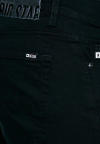 Czarne dżinsy z denimu, zbliżenie na tylną kieszeń z etykietami "BIG STAR" i widocznymi detalami szwów.