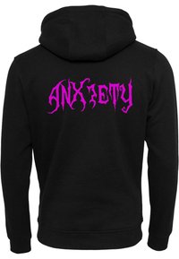 Crna dukserica s kapuljačom, na leđima ima veliki ružičasti natpis "ANXIETY" u stiliziranom fontu. Mekani materijal s rebrastim manžetama i rubom.