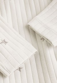 Close-up of cream ribbed fabric with stitched cuffs featuring small gray star patterns on sleeves.