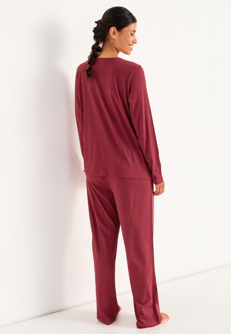 Bordeaux loungewear-set som består av en långärmad topp och löst sittande byxor, tillverkad av mjukt tyg med en slät yta. Enkel design och avslappnad passform.