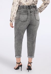 Šedé denimové kalhoty s vysokým elastickým pasem, manžetami a zadními kapsami. Textura má vybledlý, opotřebovaný vzhled.