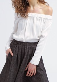 Blusa blanca sin mangas con un escote plisado, combinada con una falda gris de talle alto y fluida que tiene una textura suave.