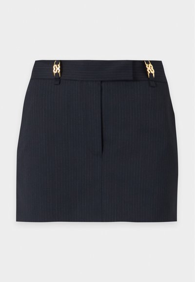 Mini-jupe noire à fines rayures avec couture avant et clips décoratifs dorés à la taille sur fond blanc.