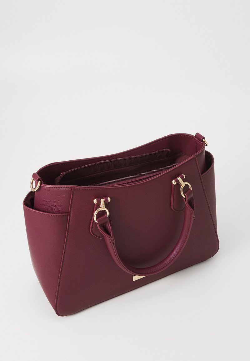 Bolso burdeos hecho de material sintético texturizado. Presenta herrajes en tono dorado, dos asas superiores y un compartimento principal con cremallera.