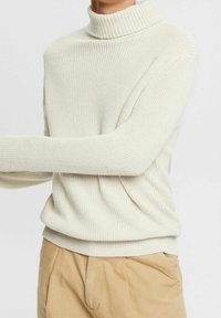Cremefarbener Rollkragenpullover in strukturierter Strickoptik mit geripptem Kragen und Saum. Wird über beige Hosen getragen, mit lockeren Ärmeln.