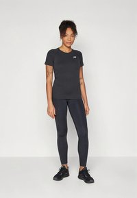 Schwarzes Sport-T-Shirt mit rundem Halsausschnitt und kurzen Ärmeln, kombiniert mit hoch taillierten schwarzen Leggings. Auf dem Shirt befindet sich ein kleines Logo.