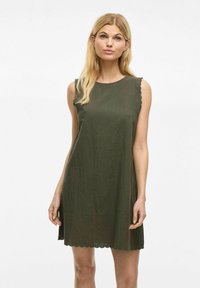 Vestido sin mangas de color verde oliva, hecho de un tejido texturizado, que presenta bordes en forma de onda en las sisas y el dobladillo, con una silueta holgada.
