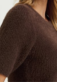 Brun, fluffig stickad tröja med korta ärmar och vid halsringning, med en texturerad yta och mjuk känsla.