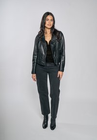 Czarna skórzana kurtka motocyklowa na czarnym dopasowanym topie i ciemnych dżinsach, zestawiona z czarnymi botkami na obcasie. Gładka faktura, dopasowany fason.
