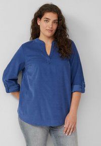 Blaue Bluse mit langen Ärmeln, V-Ausschnitt und aufgerollten Manschetten. Der Stoff scheint glatt zu sein; sie hat eine lässige Passform und einen abgerundeten Saum.