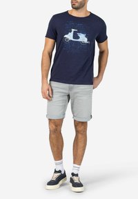 Navy blue cotton t-shirt with a scooter graphic, paired with light grey denim shorts folded at the hem and dark sneakers with white soles.