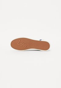 Rubber sole with a wave pattern, tan color, and white rim. Features "Lee" logo embossed on the bottom, indicating brand.