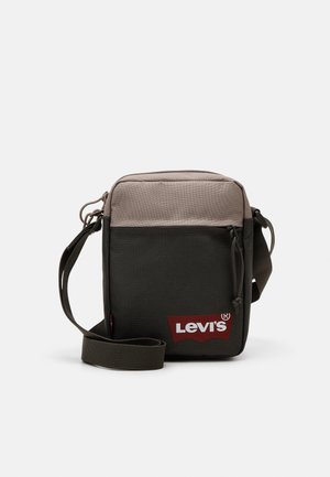 Mała, prostokątna torba na ramię z dwukolorowego materiału w beżu i czerni, przednia kieszeń na zamek, regulowany pasek oraz czerwone logo Levi's z przodu.